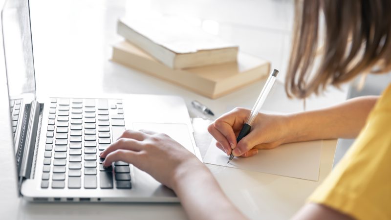 A teenage girl doing homework sitting with books and laptop, online learning concept, child studying at home.